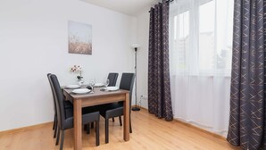Un comedor con una mesa de madera dispuesta para cuatro, sillas negras, un florero con flores y un cuadro en la pared.