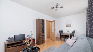 Una sala de estar moderna con un sofá gris, mueble de entretenimiento de madera y un comedor con mesa y sillas.