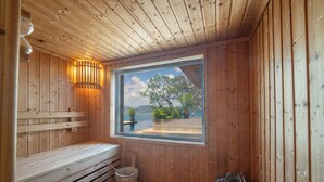 Eine Holzsauna mit Bänken, einem Fenster mit Blick auf Grünflächen und Berge sowie einem Eimer.