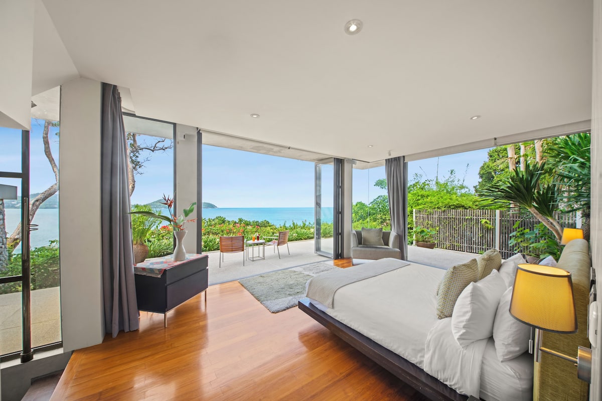 Quarto moderno com uma cama grande, uma escrivaninha e vista para o mar.