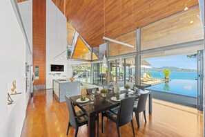 Ein moderner Essbereich mit Holzboden, großen Fenstern und Blick auf Pool und Meer.