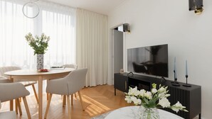 A modern living room with a round dining table, two chairs, a TV, and a black entertainment unit.