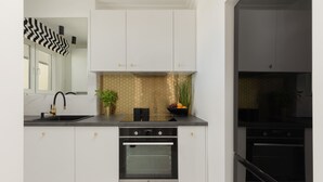 A modern kitchen with white cabinets, a black countertop, a built-in oven, and a backsplash with a honeycomb pattern.
