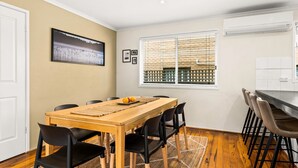 Een eethoek met een houten tafel, zwarte stoelen, een vloerkleed en een raam met luxaflex.