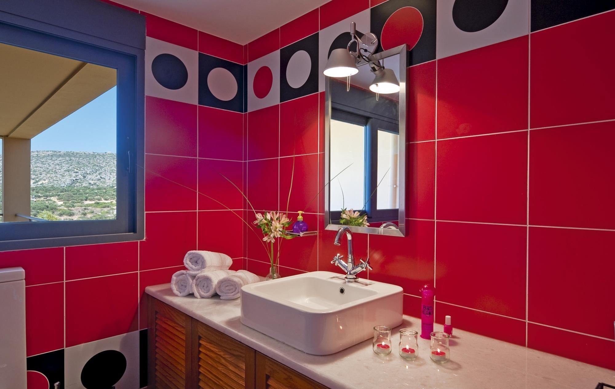 A bathroom with red tiles, a white sink, and a window with a view of a landscape.