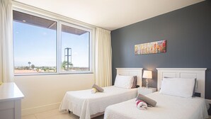 Una habitación de hotel con dos camas, un ventanal con vistas, un cuadro en la pared y un escritorio con una lámpara.