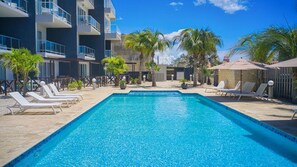 Piscina retangular com águas cristalinas azuis, rodeada por espreguiçadeiras e palmeiras.