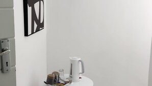 Habitació minimalista amb una taula blanca, una cafetera i una obra d'art abstracta emmarcada a la paret.