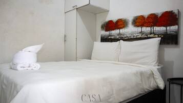 A hotel room with a neatly made bed, a painting of autumn trees on the wall, and a folded towel on the bed.
