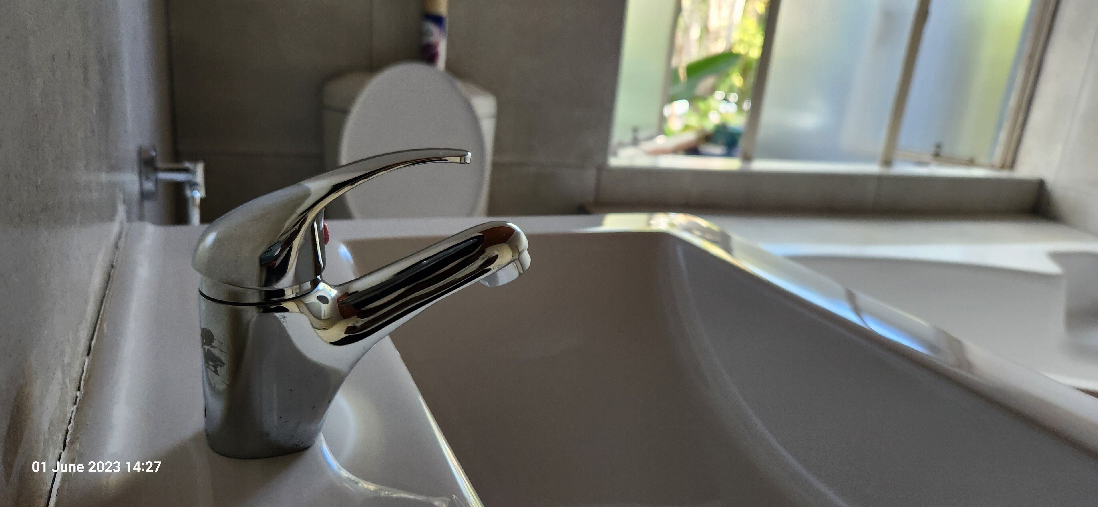 A bathroom with a chrome faucet, a white sink, and a window with a view of greenery.