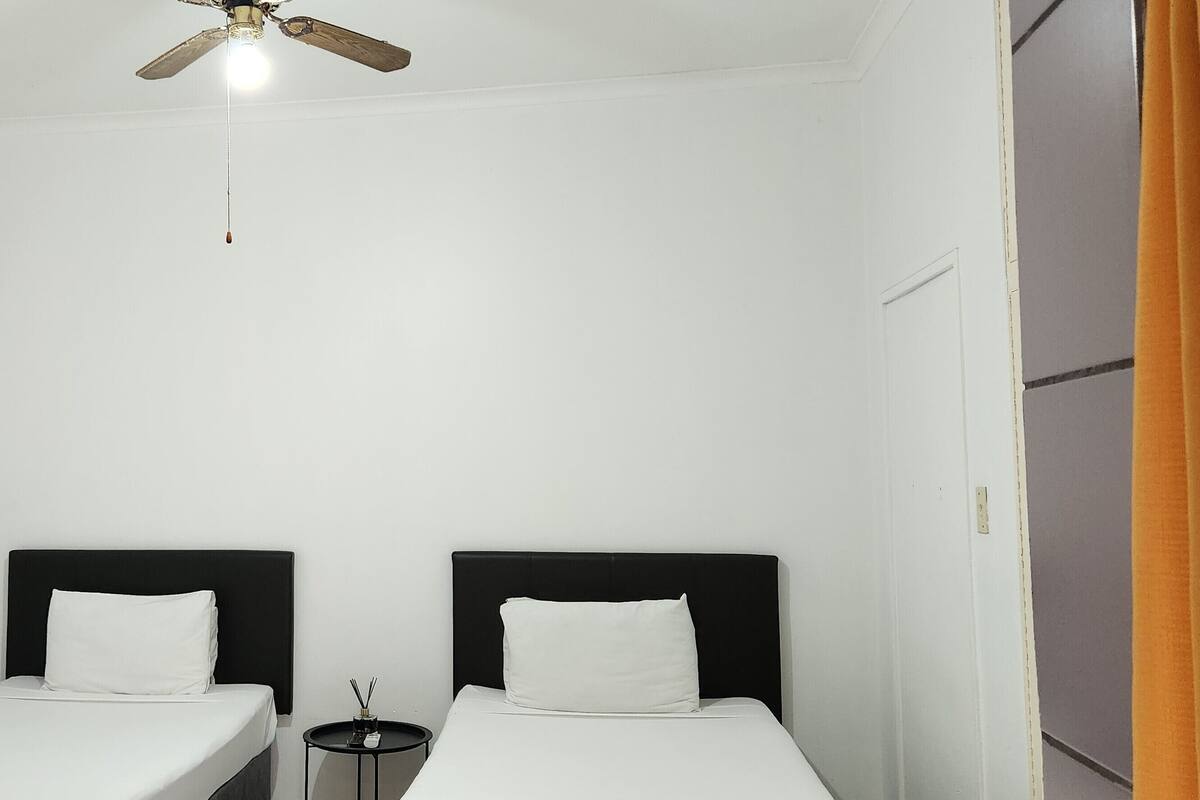 Una habitación con dos camas individuales, un ventilador de techo y una pequeña mesa con lámpara.