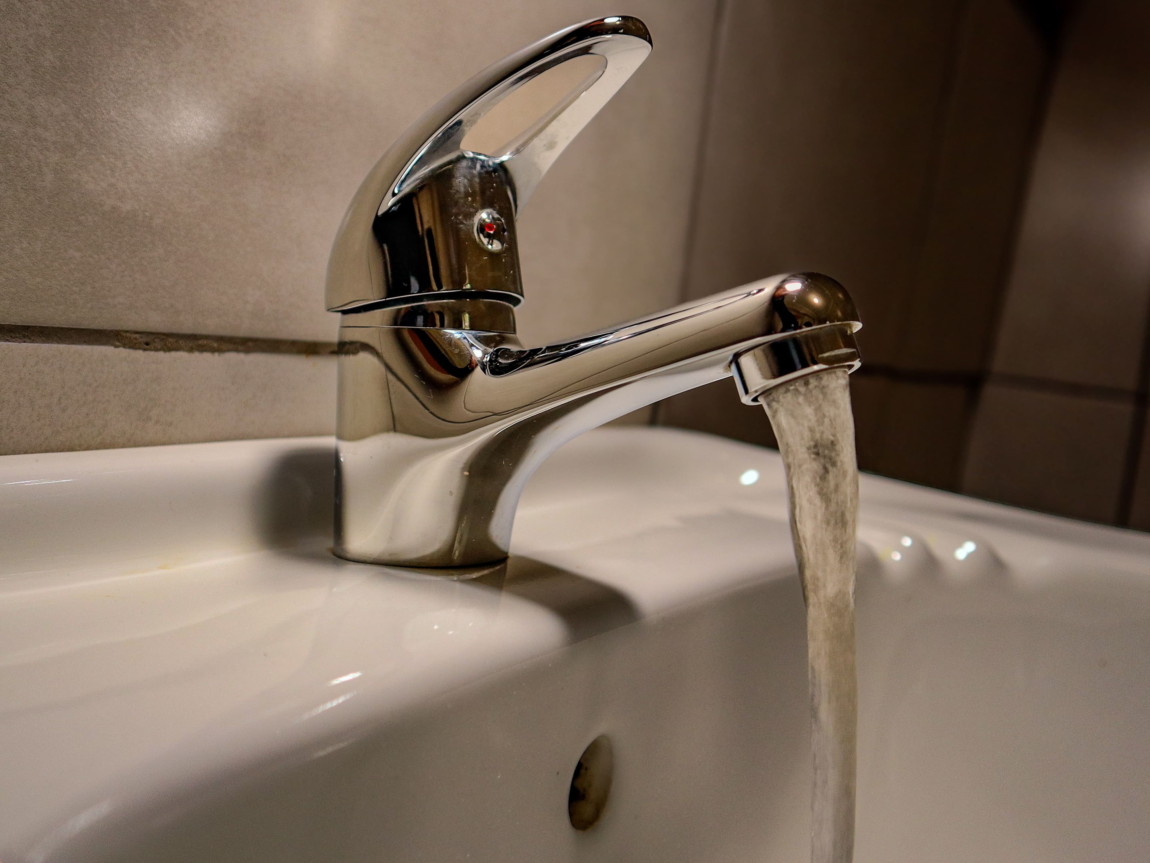 Un grifo cromado con agua corriendo en un lavabo blanco.