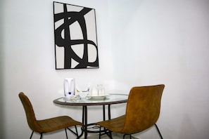 Et værelse med et rundt bord, to stole, en kaffemaskine og et glas vand.