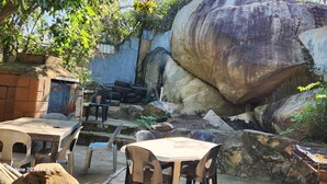 Un espace extérieur aménagé avec des tables et des chaises, entouré de gros rochers et d’un mur en béton.