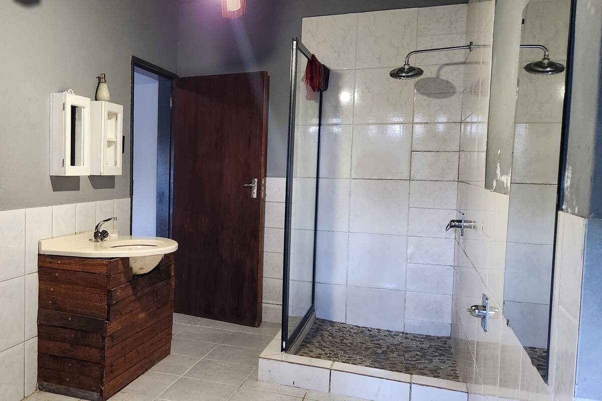 Un baño con tocador de madera, lavamanos, armario, ducha con puerta de vidrio y puerta con manija.