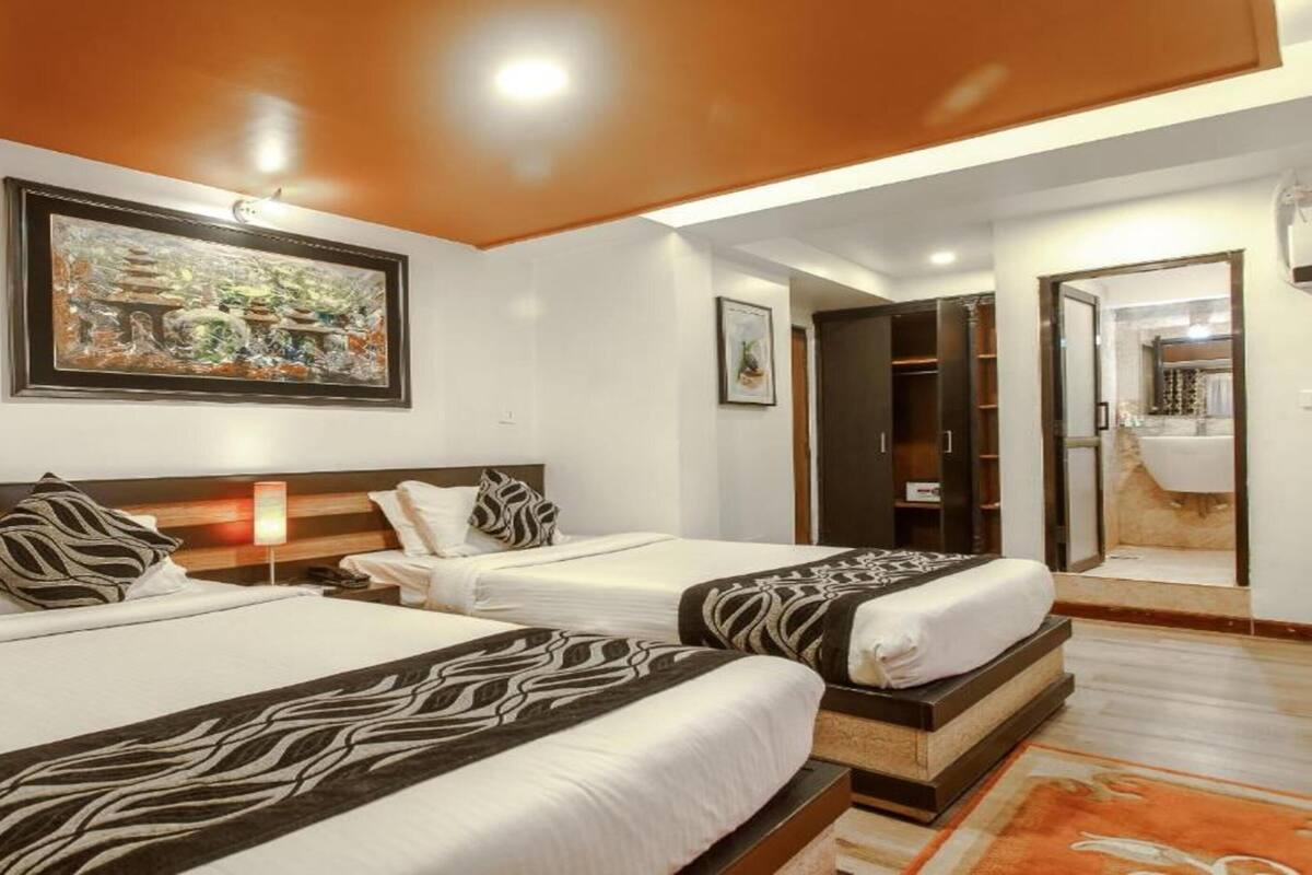 A hotel room with two beds, a large painting on the wall, a wardrobe, and a bathroom visible through an open door.