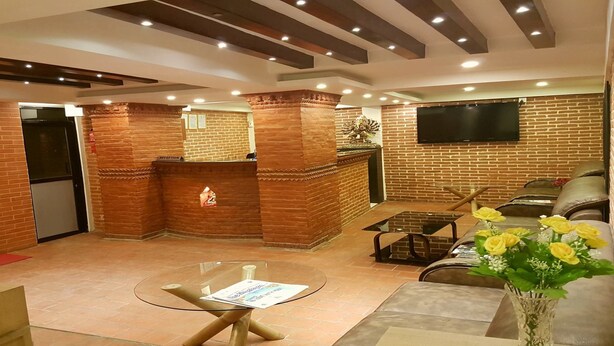 A lobby with a reception desk, a glass table, a sofa, and a TV mounted on the brick wall. - MeroStay 179 Shree (Kathmandu)