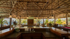 A restaurant with a thatched roof, wooden furniture, and a view of the sea. - Exclusive Private Island With 360 Degree View of the Ocean (Placencia)