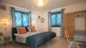 A bedroom with a bed, a desk, and a chair. There are curtains on the windows, a wall-mounted light, and a hanging plant. - NEW Cozy Casa in Oranjestad (Oranjestad)