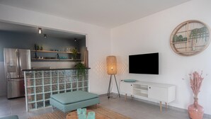 A modern living room with a sofa, a coffee table, a TV, and a kitchen area with a fridge and shelves. - NEW Cozy Casa in Oranjestad (Oranjestad)