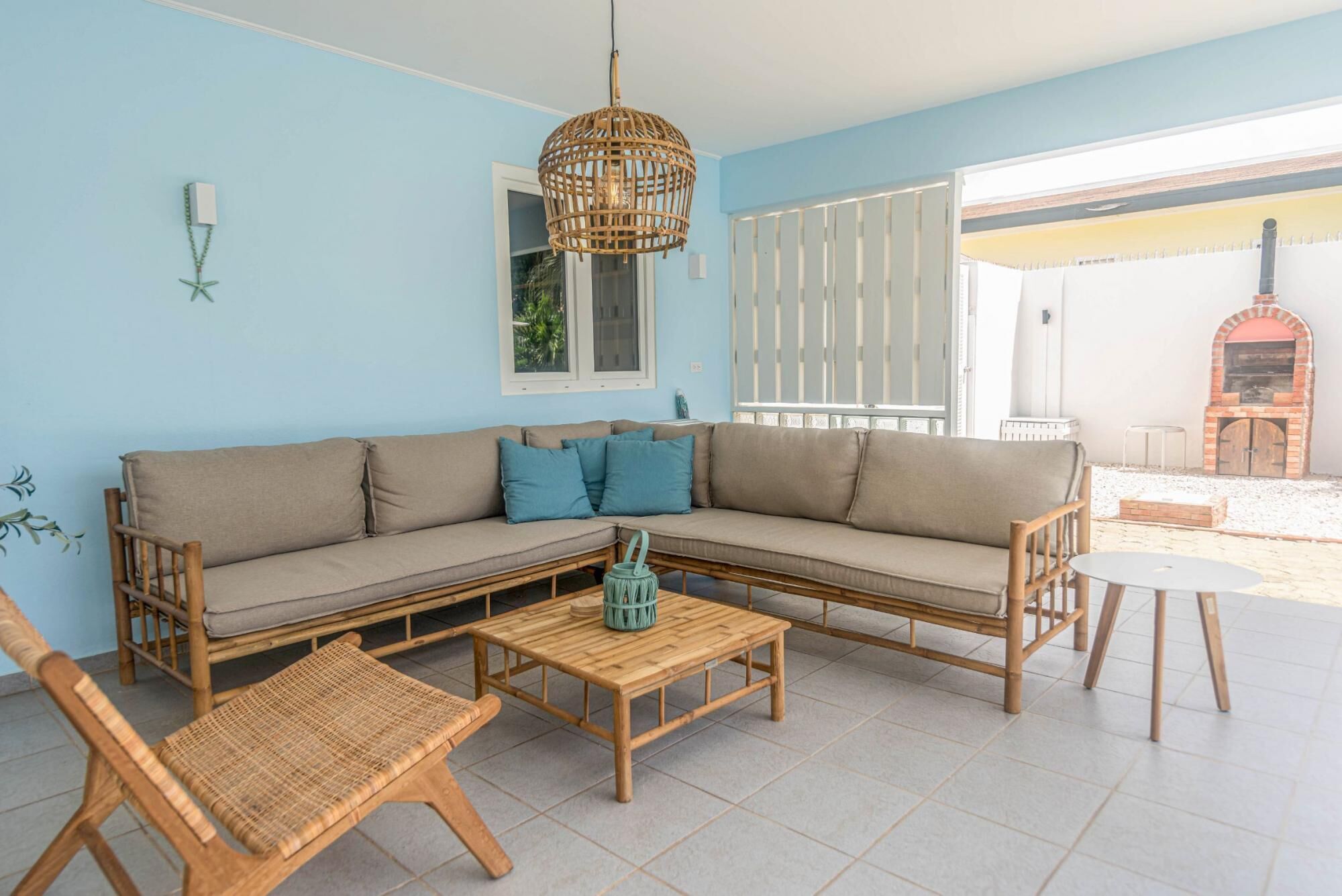 Una sala de estar con un sofá seccional color beige, dos sillas de madera, una mesa de centro de madera y una lámpara colgante de mimbre.