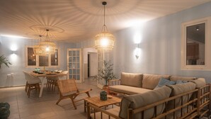 A spacious living area with a sofa, chairs, and a dining table. There are two hanging light fixtures and a potted plant. - NEW Cozy Casa in Oranjestad (Oranjestad)