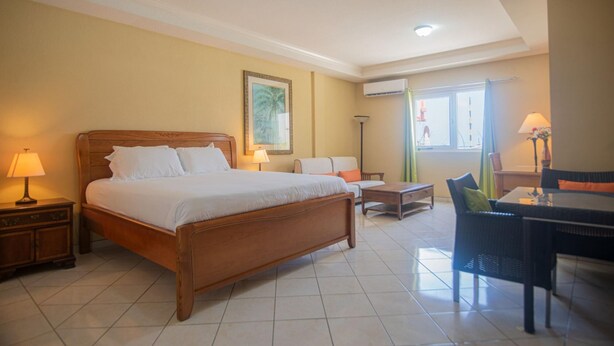 A hotel room with a large bed, a desk, a chair, a sofa, and a lamp. - NEW Bay Harbor Studio 202 (Oranjestad)