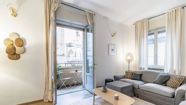 A modern living room with a grey sofa, a small wooden coffee table, and a balcony with a view of the city. - Apartment in Milan with 3 bedrooms sleeps 8 (Milan)
