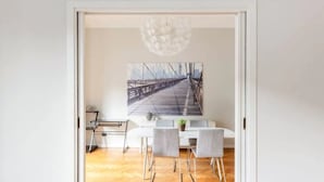 A dining area with a table and chairs, a hanging light fixture, and a large painting of a bridge.