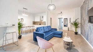 A modern living room with a blue sectional sofa, a pink chair, and a small round table. There is a kitchen in the background with white cabinets and a dining area with white chairs. - Apartment in Milan with 4 bedrooms sleeps 7 (Milan)