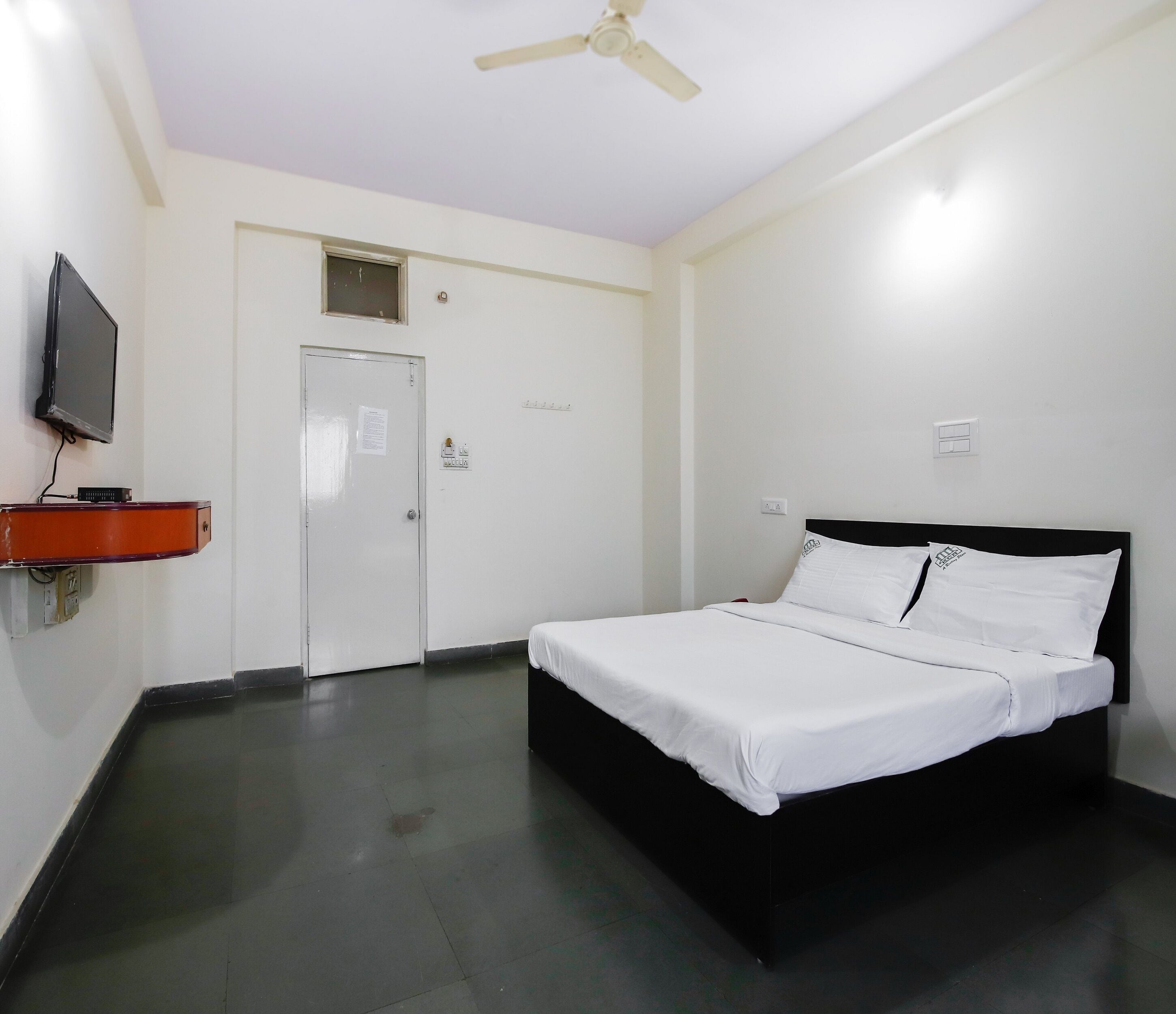 A bedroom with a bed, a television, a ceiling fan, and a door.