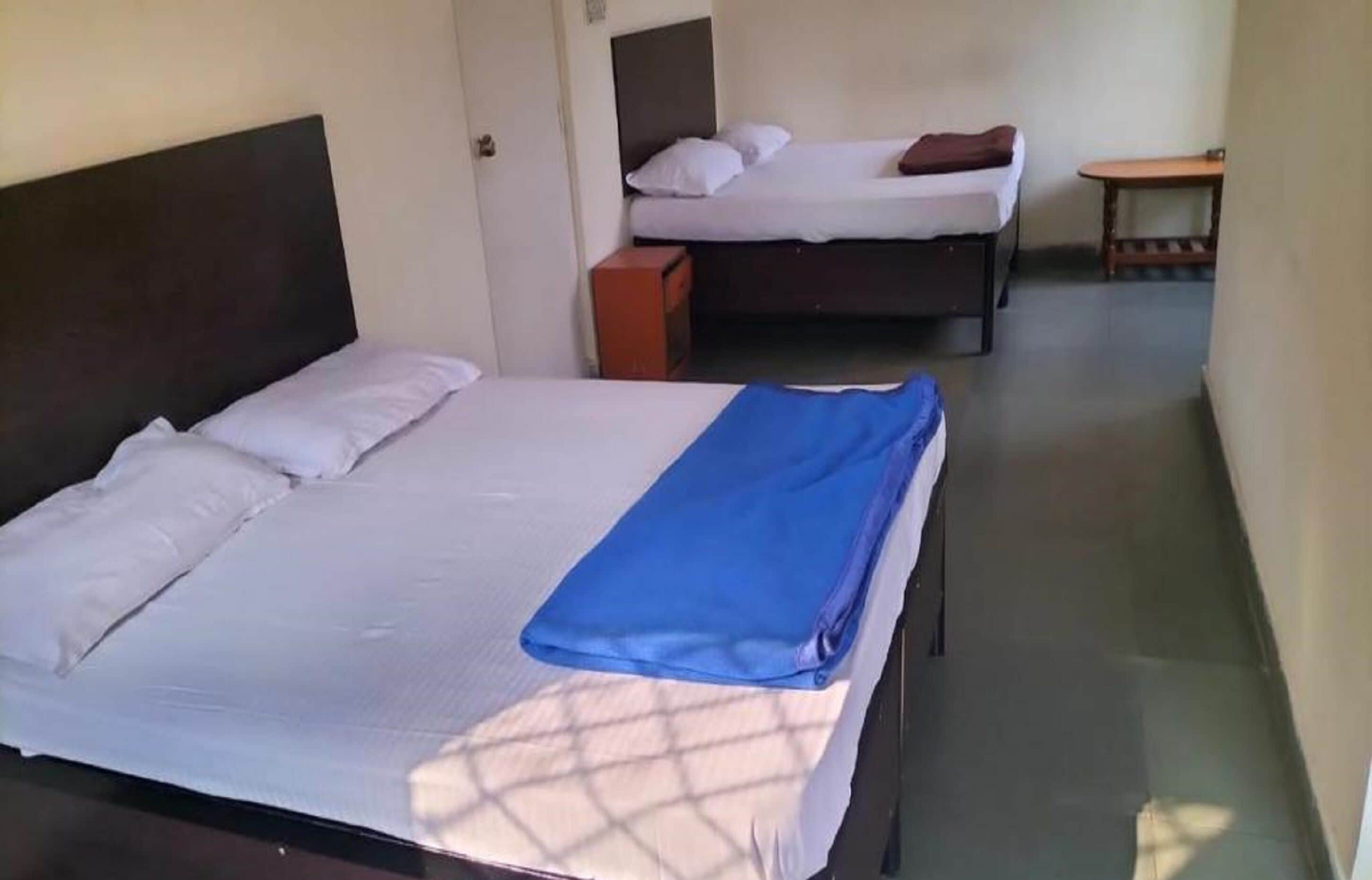 A hotel room with two beds, a small table, and a bench.