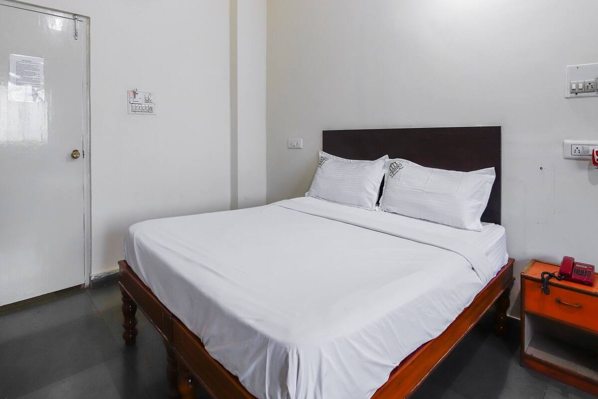 A single bed with a wooden headboard, white bedding, and a bedside table with a red telephone.