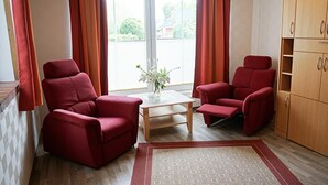 A room with two red armchairs, a wooden table, and a cabinet.