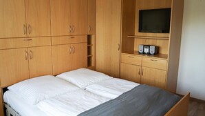 A bedroom with a bed, wooden wardrobe, and a television on a shelf.