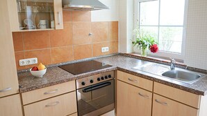A kitchen with a stove, oven, sink, and a bowl of fruit on the counter.