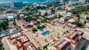 An aerial view of a coastal residential area with multiple buildings, a central swimming pool, and a beach. - Narcissos Nissi Beach Apartment A8 (Ayia Napa)