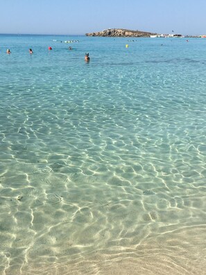 A beach with clear shallow water and a rocky outcrop in the distance. - Narcissos Nissi Beach Apartment A8 (Ayia Napa)
