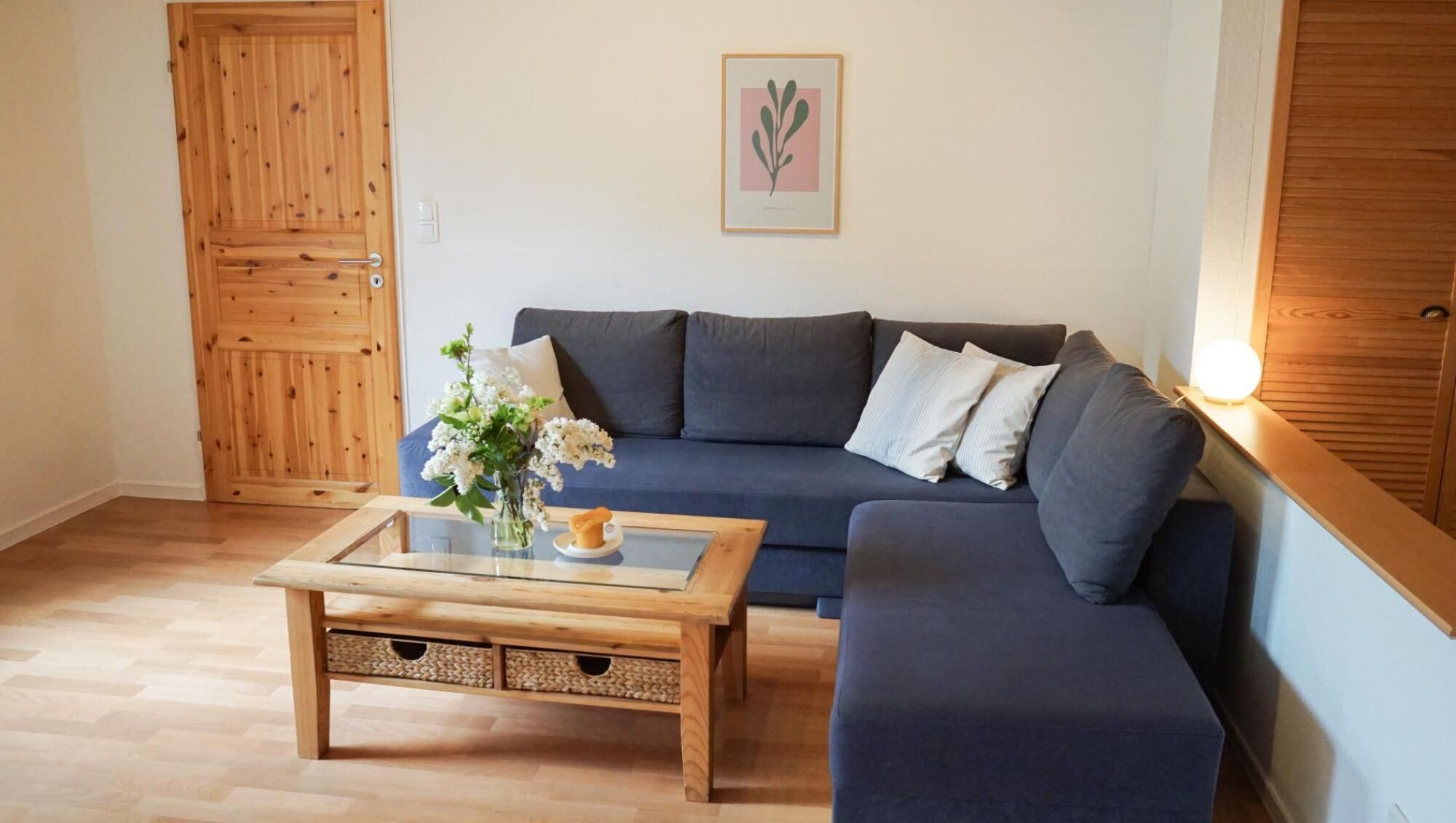 A living room with a dark blue sofa, a wooden coffee table with a vase of flowers, and a wooden door.
