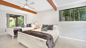 A bedroom with two beds, a ceiling fan, a window with a view of greenery, and a brick wall. - Fields of Green by Experience Jervis Bay (Vincentia)