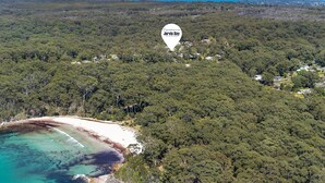 An aerial view of a coastal area with dense forest, a beach, and scattered houses. - Fields of Green by Experience Jervis Bay (Vincentia)