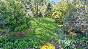 A well-maintained garden with a variety of trees and shrubs, a neatly trimmed lawn, and a stone pathway. - Fields of Green by Experience Jervis Bay (Vincentia)