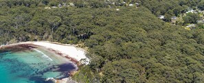 An aerial view of a coastal area with dense forest, a beach, and scattered houses.