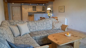 A cozy living room with a patterned sofa, a wooden coffee table, and a kitchen in the background. - Ferienwohnung Leuchtturm (Fehmarn)