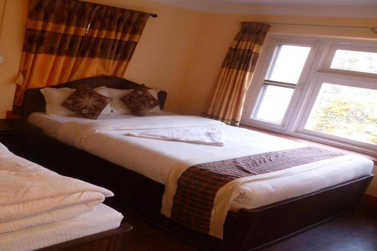 Ein Hotelzimmer mit zwei Betten, einem Fenster mit Vorhängen und Blick ins Freie.