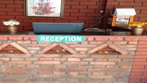 En receptionsdisk med en skylt som visar ”RECEPTION”, en bärbar dator, en insamlingslåda och en vas med blommor.