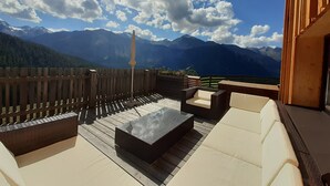 A deck with outdoor seating, a table, and a view of mountains. - Studio in Ötztal with wellness, children's playground and farm (Umhausen)