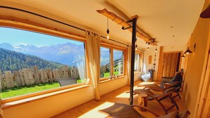 A sunlit room with wooden furniture, large windows, and a view of mountains. - Studio in Ötztal with wellness, children's playground and farm (Umhausen)
