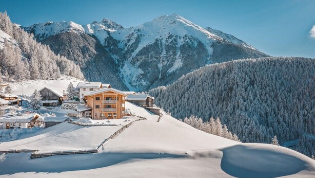 A snow-covered mountain village with wooden buildings, a ski slope, and a clear blue sky. - Studio in Ötztal with wellness, children's playground and farm (Umhausen)