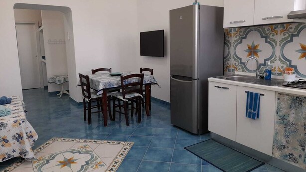 Une cuisine compacte comprenant un réfrigérateur, une table à manger avec des chaises, un petit évier et un plan de travail carrelé.